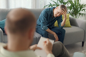 Das Foto zeigt einen Mann auf einer Couch sitzend im Gespr&auml;ch mit seinem Psychotherapeuten.