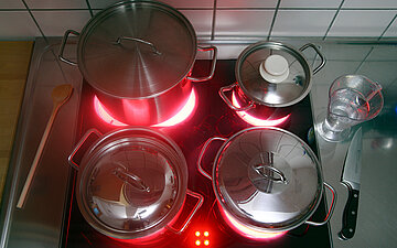Foto: Auf einer Einem Elektroherd stehen vier Töpfe. Die Herplatten glühen rot.