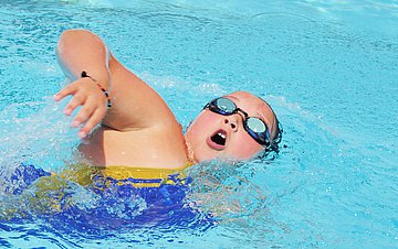 Adipositas bei Kindern Foto eines korpulenten Jungen, der mit Schwimmbrille im Schwimmbad krault