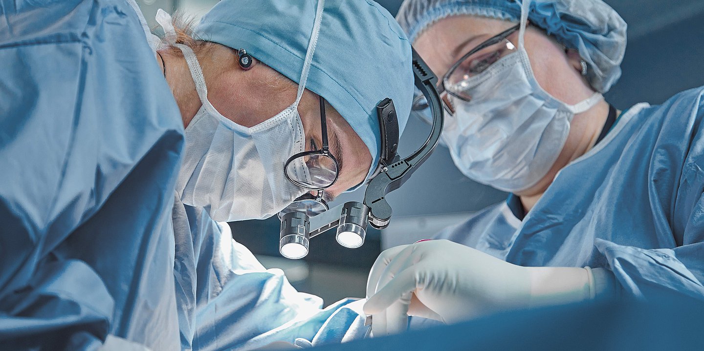 Foto: Ein OP-Team in OP-Kleidung und mit Mund-Nasen-Schutz operiert einen Patienten.