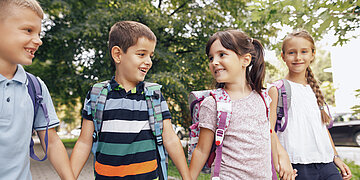  Schulkinder mit fr&ouml;hlichen Gesichtern halten sich an den H&auml;nden