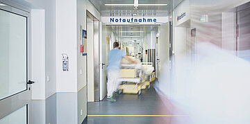Ein Pfleger schiebt ein Bett den Flur der Notaufnahme eines Krankenhauses entlang.