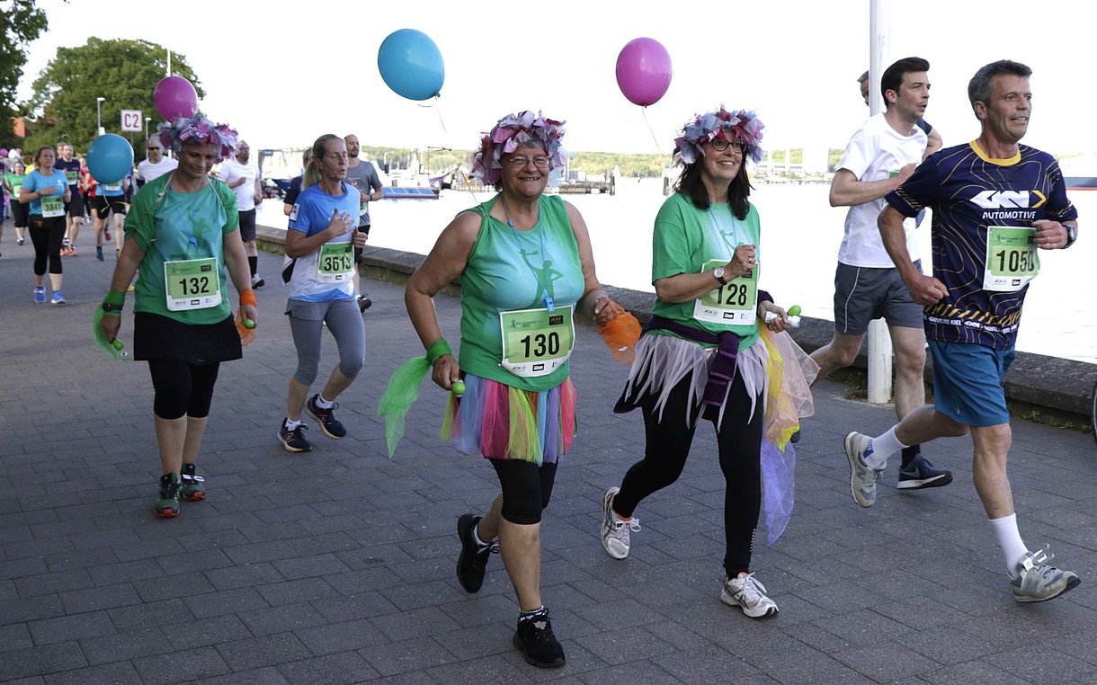 Lauffreudige Teams in kreativen Outfits laufen gut gelaunt an der Kiellinie entlang