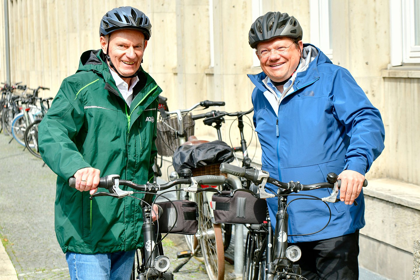 Foto: Vorstandsvorsitzender Dr. Jürgen Peter (links) und Sozial- und Gesundheitsminister Dr. Andreas Philippi stehen draußen nebeneinander mit ihren Fahrrädern in der Hand und Fahrradhelmen auf dem Kopf