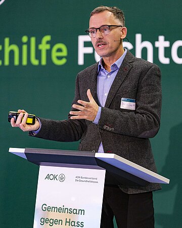 Prof. Ludwig Bilz steht an einem Rednerpult und gestikuliert.