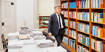 Giovanni Maio steht in einem B&uuml;ro vor einem B&uuml;cherregal mit Fachliteratur