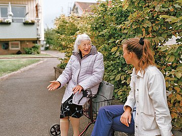 Pflegequalität Foto einer alten Dame mit Rollator, die im Freien mit einer jungen Frau spricht