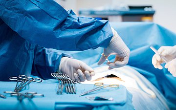 Operateur näht Operateur und Assistent schließen eine OP-Wunde mit einem Faden (Ausschnitt der Hände) im Vordergrund weiteres OP-Besteck