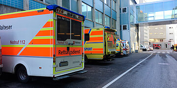 Parkplatz neben einem Krankenhaus. Mehrere Rettungswagen in verschiedenen Gr&ouml;&szlig;en stehen nebeneinander.