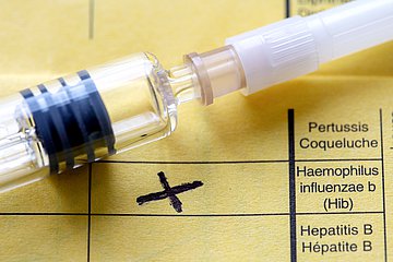 Eine Spritze liegt auf einem Impfpass. Es handelt sich um eine Hib-Impfung.