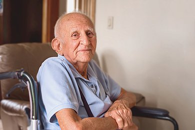 Foto: Ein alter Mann sitzt in einem Rollstuhl und schaut in die Kamera.