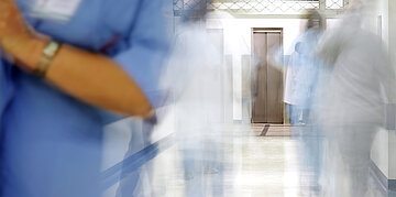 In einer verschwommenen Ansicht zeigt das Bild einen Krankenhausflur, &uuml;ber das verschiedenes medizinisches Personal geht. Durch die Verschwommenheit sieht es aus, als w&uuml;rden sie sich bewegen.