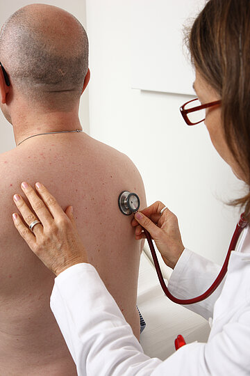 Eine &Auml;rztin h&ouml;rt mit einem Stethoskop einen Patienten ab. 