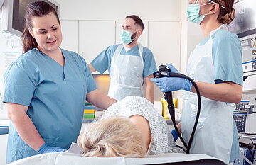 Ein &Auml;rzteteam und Krankenpfleger f&uuml;hren im Krankenhaus eine Koloskopie an einer Patientin durch. Der Arzt verfolgt die Koloskopie auf dem Bildschirm. 