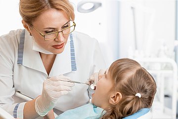 Zahnprophylaxe bei Kindern Ein Kind sitzt mit geöffnetem Mund beim Zahnarzt.