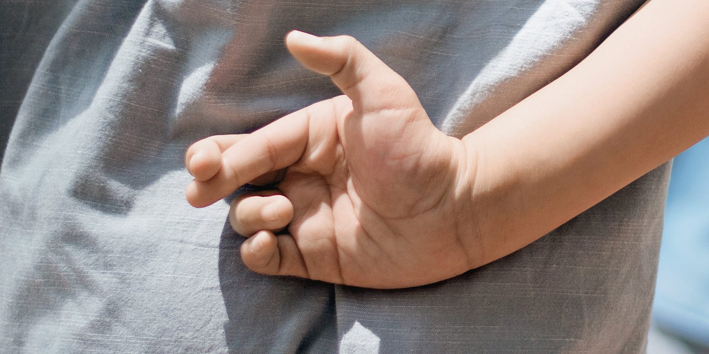 Foto: Ein Person kreuzt die Finger hinter dem Rücken.