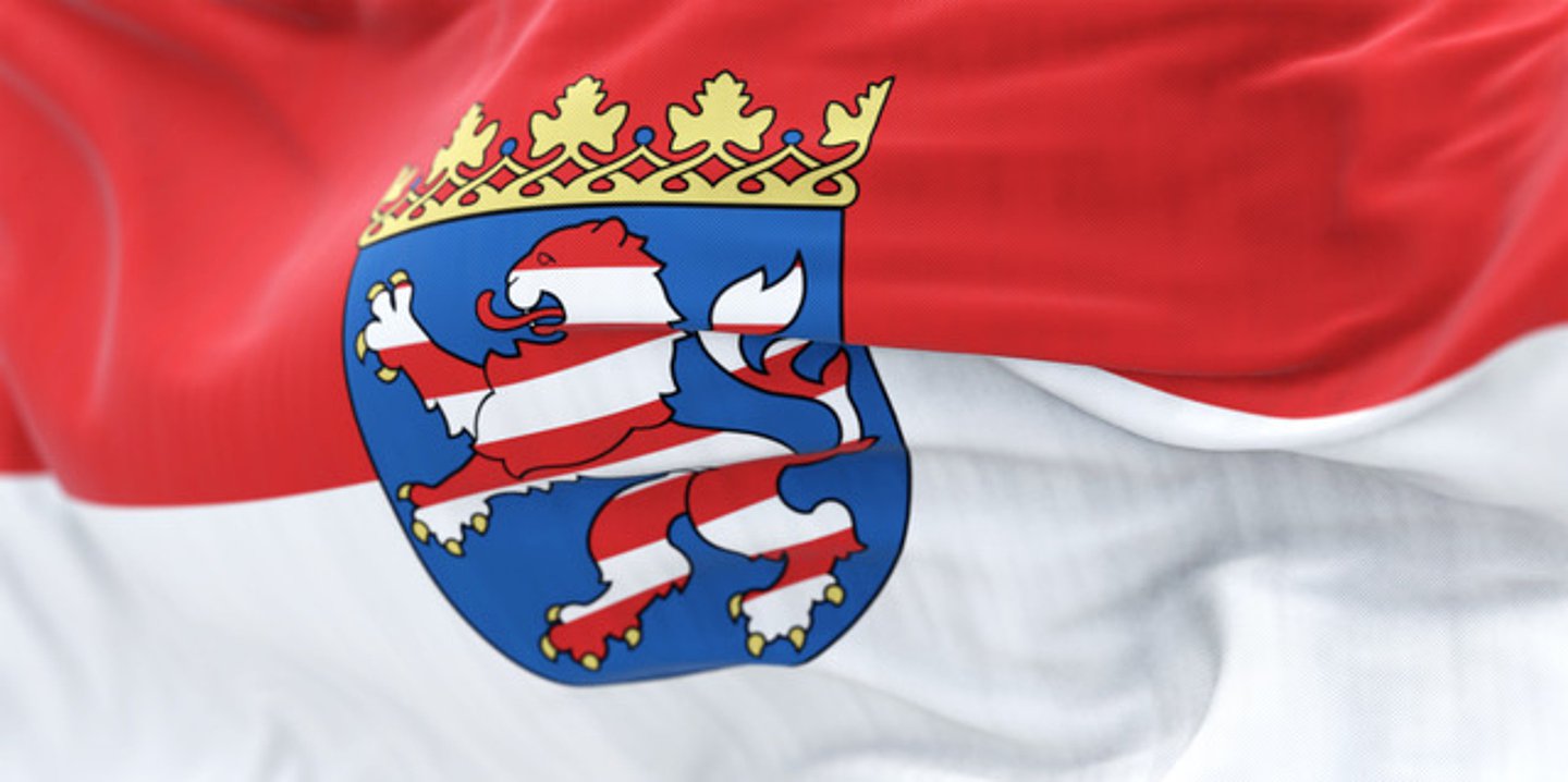 Foto: Rot-weiße, quergesteifte, hessische Landesfahne im Wind, in der Mitte das Landeswappen mit stehendem rot-weißen, quergestreiften Löwen auf blauem Grund 