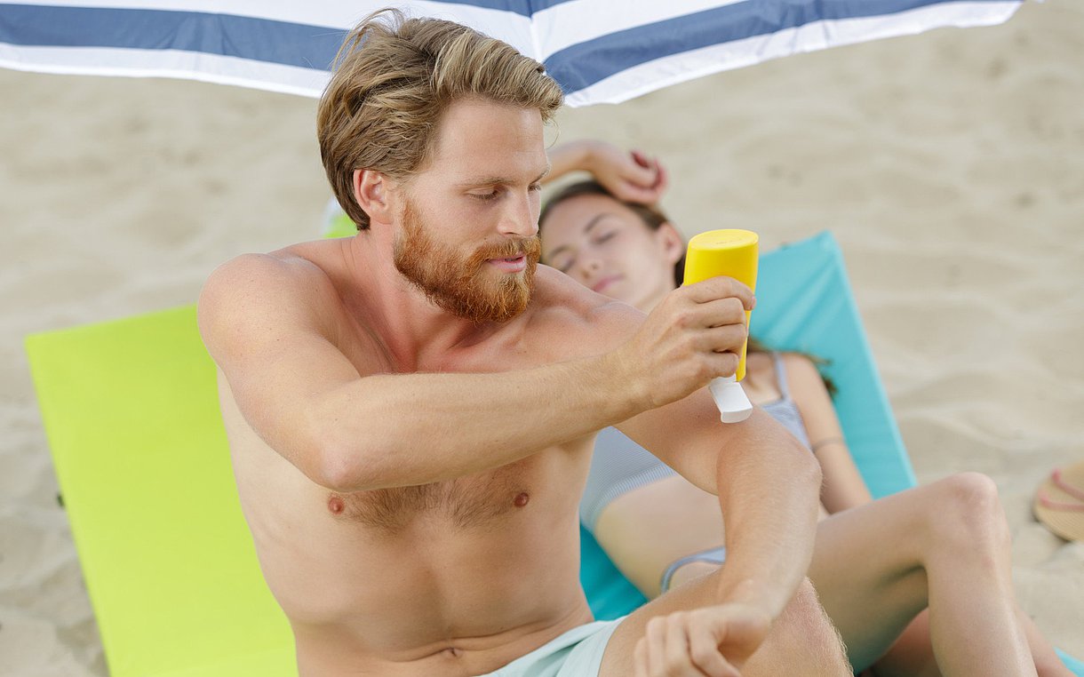 Foto: Ein Mann cremt sich am Strand ein.