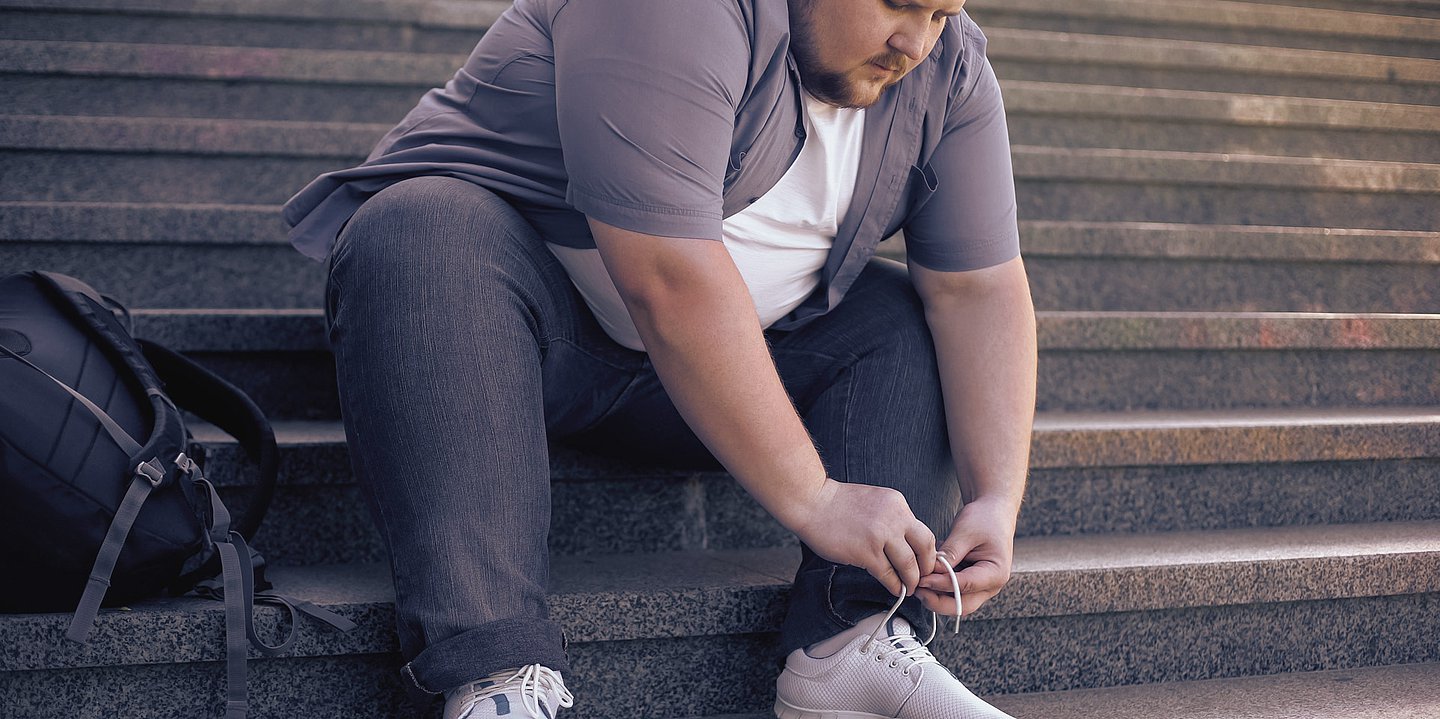Foto: Ein übergewichtiger Mann beugt sich nach vorne, um seinen Schuh zu binden.