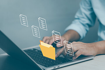 &Uuml;ber einem aufgeklappten Laptop schweben transparente Aktensymbole, w&auml;hrend jemand auf der Tastatur tippt.