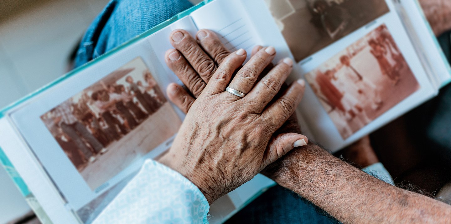Foto: Die Hände eines älteren Menschen liegen überkreuzt auf einem aufgeschlagenen Fotoalbum.