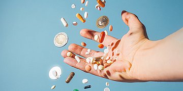 Arzneimittel Bild einer Hand, die Tabletten auffängt vor hellblauem Hintergrund