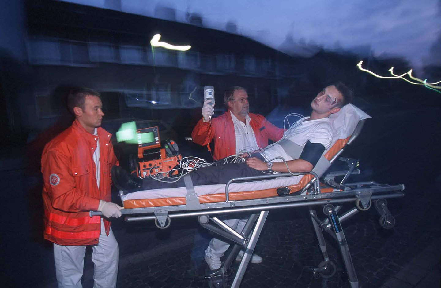 Zwei Rettungssanitäter bringen einen Verletzten mit einer fahrbaren Trage in einen Rettungswagen.