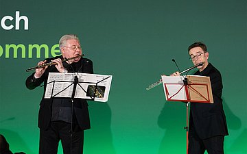 Zwei Personen spielen Querflöte auf einer Bühne.