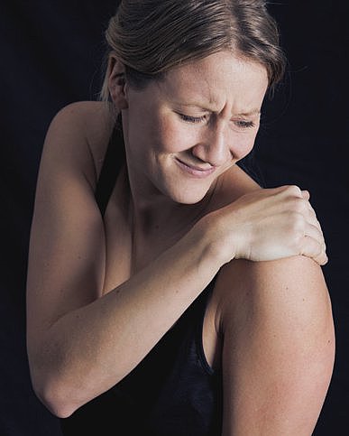Foto: Eine Frau fasst sich mit schmerzverzerrtem Gesicht an die Schulter.