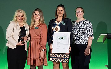 Vier Frauen stehen nebeneinander, eine hält eine Urkunde.