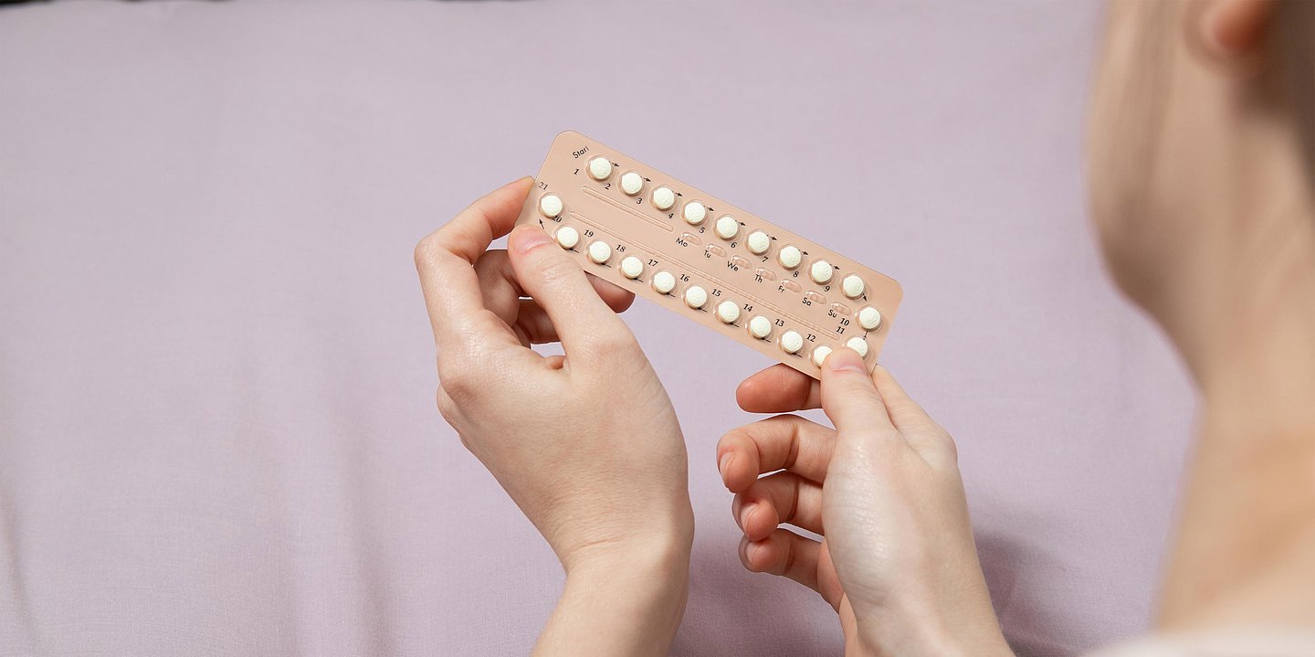 Foto zeigt eine Frau im Anschnitt, die ein Blister mit Antibabypillen in der Hand hält