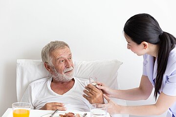 Eine Pflegekraft unterst&uuml;tzt einen Patienten im Krankenhaus beim Essen.