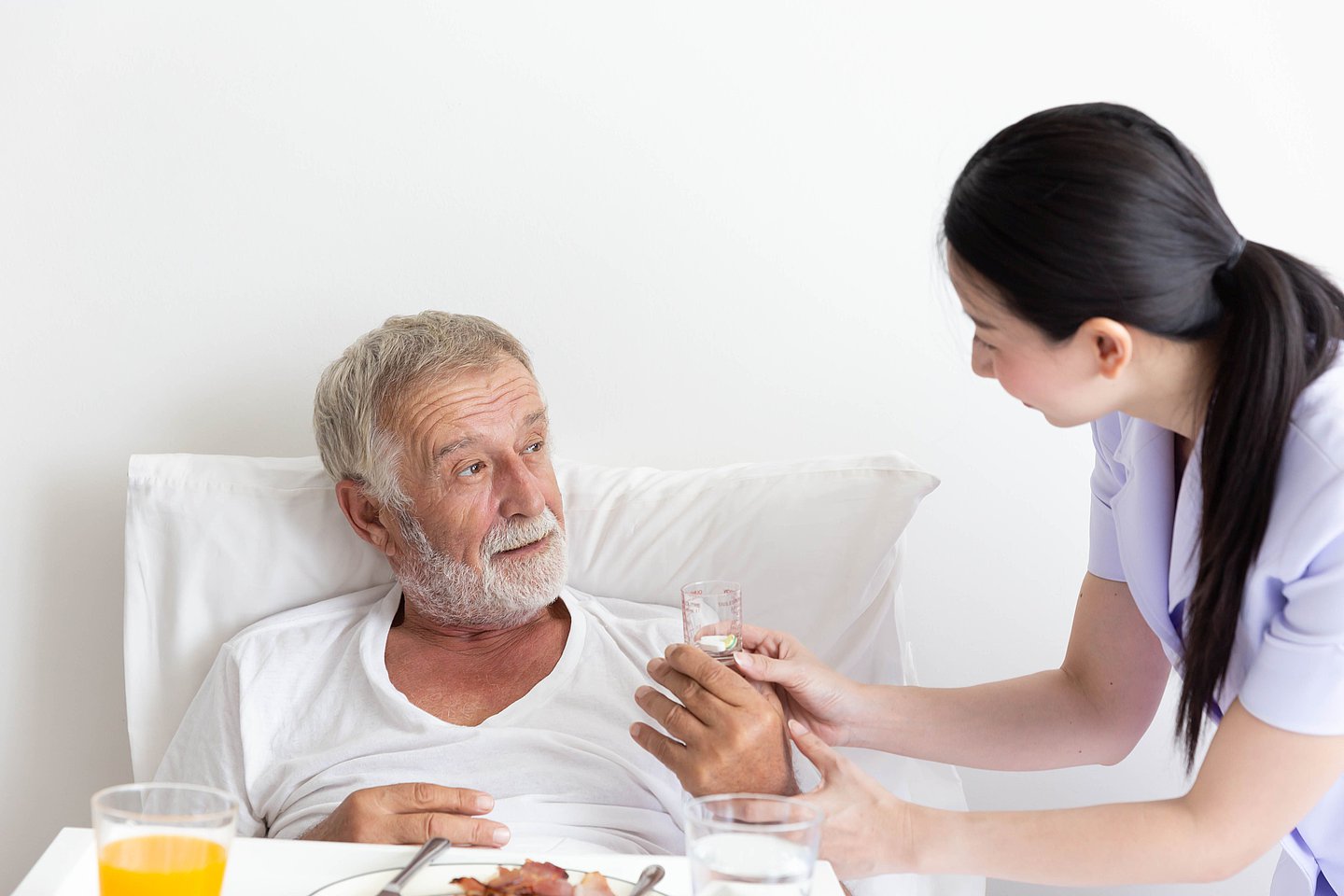 Eine Pflegekraft unterstützt einen Patienten im Krankenhaus beim Essen.