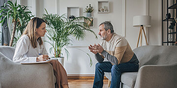 Eine Frau und ein Mann sitzen in Sesseln und reden die Frau hat einen Stift und Zettel f&uuml;r Notizen
