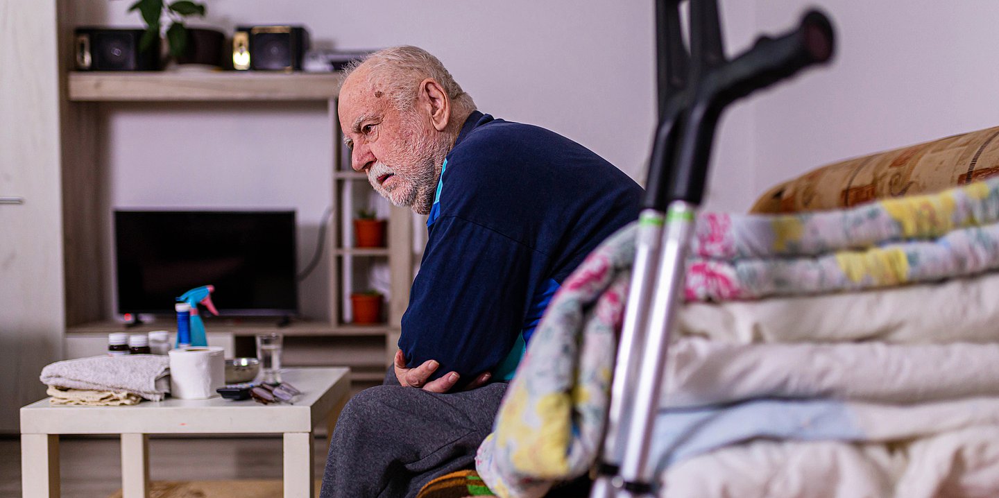 Ein älterer Mann sitzt auf einem Sofa und starrt vor sich hin.