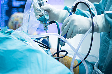 Ein Chirurg hantiert im OP-Saal w&auml;hrend der OP mit verschiedenen Ger&auml;ten am Knie eines Patienten.