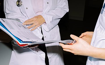 Menschen mit Behinderung Foto von zwei Medizinerinnen, die in eine Akte blicken. Die Gesichter sind nicht zu sehen.