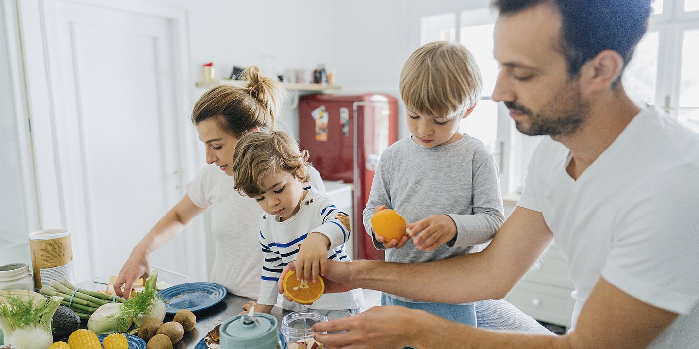 Eltern bereiten mit ihren kleinen Kindern eine gesunde Mahlzeit vor.