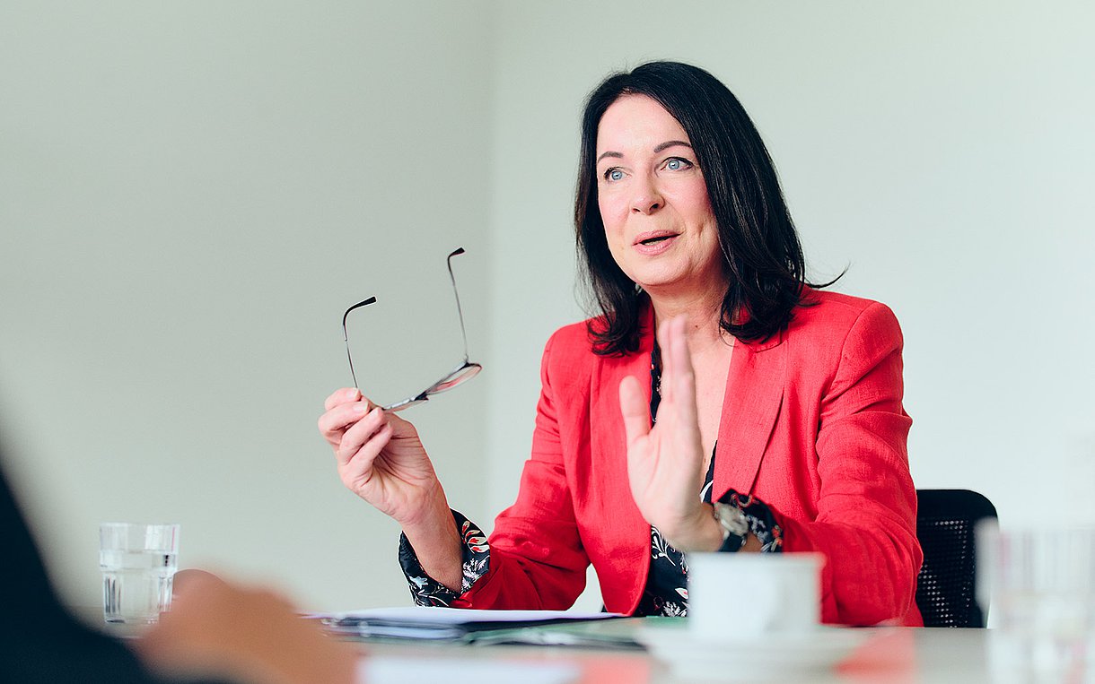 Britta Müller, Ministerin für Gesundheit und Soziales des Landes Brandenburg, am Tisch gestikulierend, mit Brille in der rechten Hand.