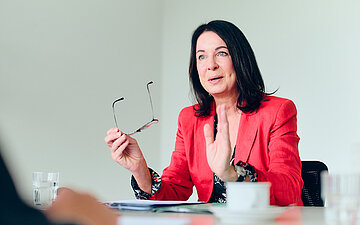 Britta M&uuml;ller, Ministerin f&uuml;r Gesundheit und Soziales des Landes Brandenburg, am Tisch gestikulierend, mit Brille in der rechten Hand.