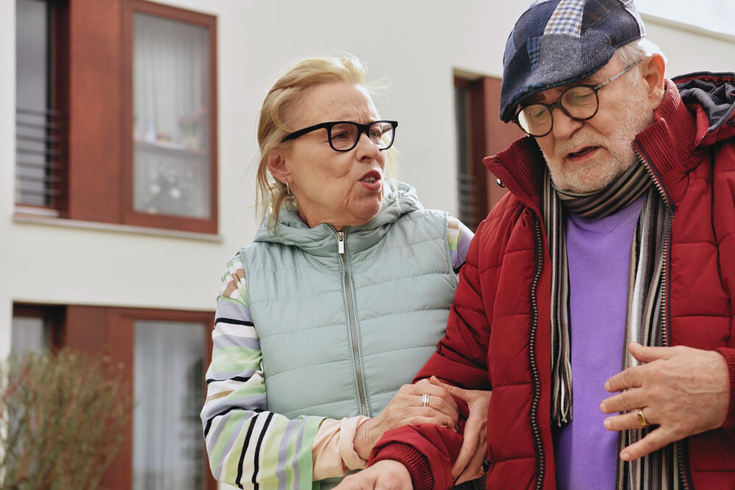 Ein älteres Paar geht nebeneinander, die Frau hält den Arm des Mannes. Dieser scheint Schmerzen zu haben und fasst sich an den Bauch.