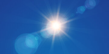 Im blauen Himmel ist die Sonne zu sehen, deren Strahlen das Licht brechen.