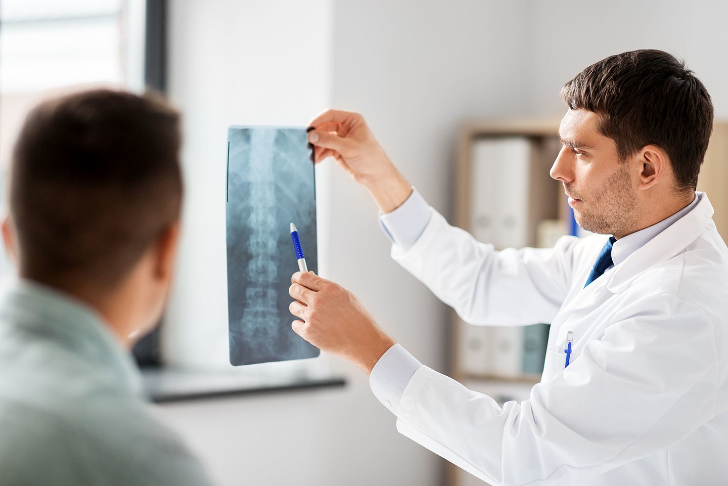 Ein Arzt zeigt einem Patienten ein Röntgenbild seiner Wirbelsäule.