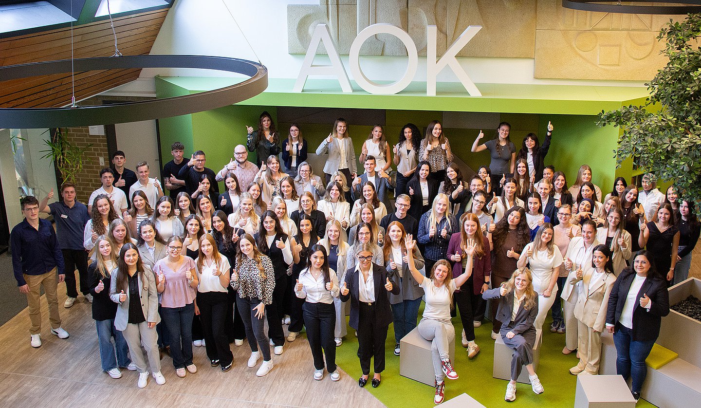 87 Auszubildende stehen und sitzen im Foyer des AOK-Bildungszentrums in Dortmund.