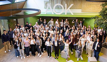 87 Auszubildende stehen und sitzen im Foyer des AOK-Bildungszentrums in Dortmund.