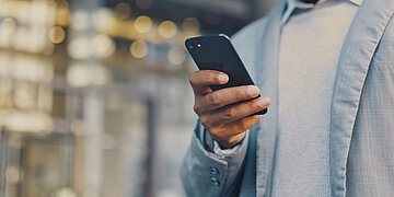 Foto: Ein Mann h&auml;lt ein Handy in der Hand. Er schaut auf das Display.