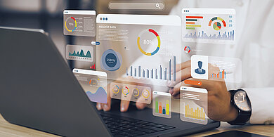 Aus einem aufgeklappten Laptop kommen Grafiken mit medizinischen Statistiken