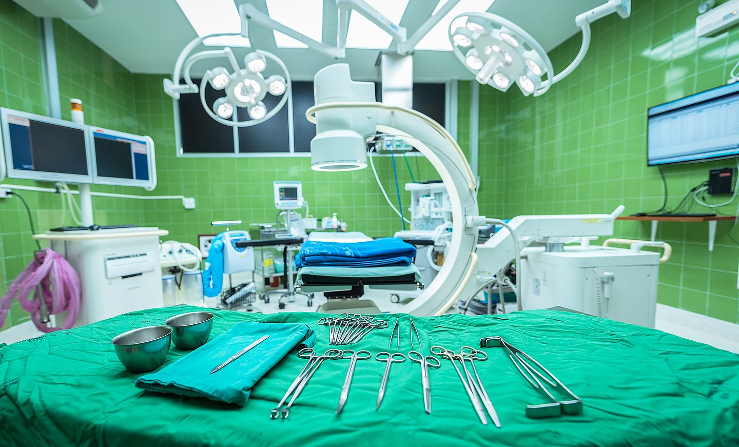 Das Foto zeigt einen OP-Raum, der für eine Operation vorbereitet ist. Im Vordergrund ist der vorbereitete Instrumententisch zu sehen, im Hintergrund der beleuchtete OP-Tisch.