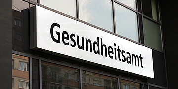 Foto zeigt den Ausschnitt einer Huasfassade und ein Schild mit der Aufschrift Gesundheitsamt
