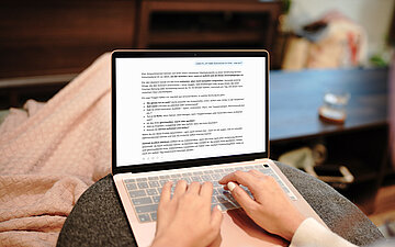 Person sitzt auf dem Sofa und nutzt ChatGPT auf einem Laptop, um sich wegen Knieschmerzen medizinischen Rat einzuholen.